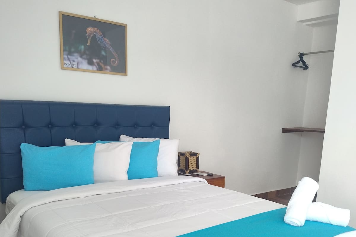 A neatly made bed with a blue and white bedspread, a blue headboard, and a framed picture on the wall.