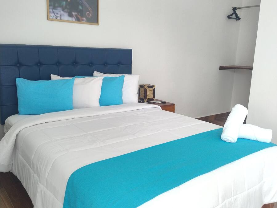 A neatly made bed with a blue and white bedspread, a blue headboard, and a framed picture on the wall.