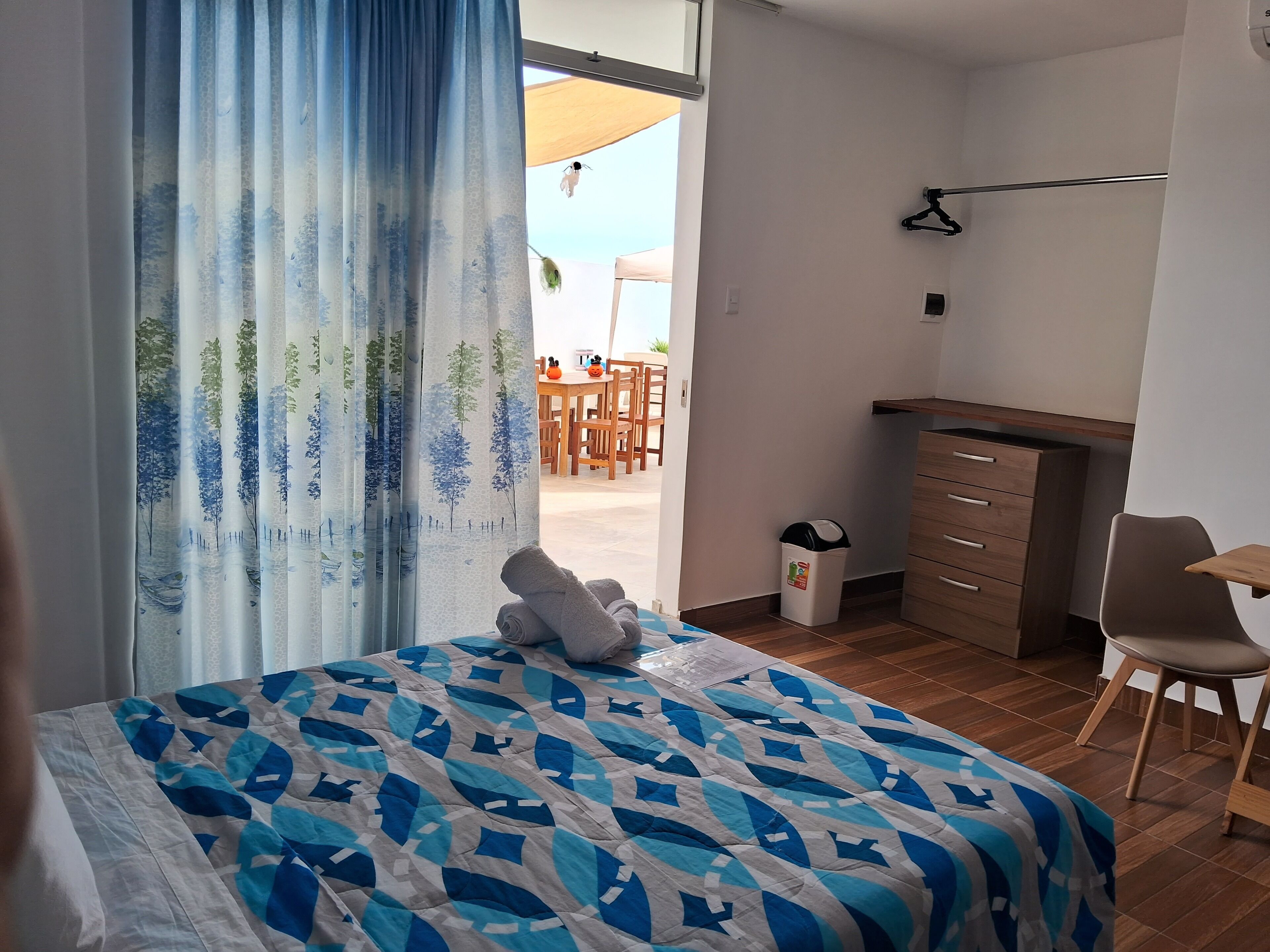 A bedroom with a bed, a desk, a chair, and a view of the outdoors.