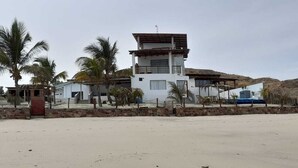 A modern two-story building with a flat roof and a balcony, surrounded by palm trees and a sandy area. - Las Fragatas Casa Hotel  (Canoas de Punta Sal)