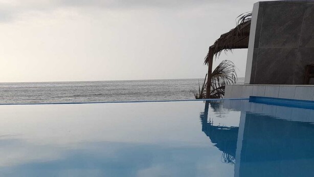 A clear view of a swimming pool with a reflection of the ocean and a building structure. - Las Fragatas Casa Hotel  (Canoas de Punta Sal)