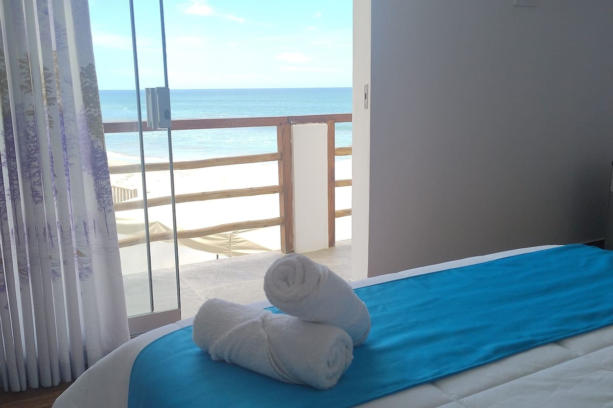 A hotel room with a bed, a view of the beach, and a balcony.