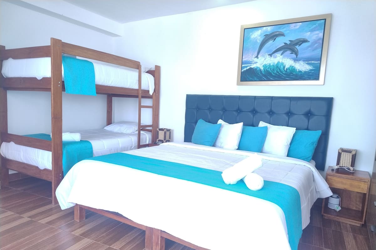 A hotel room with a bunk bed, a single bed, and a headboard with a tufted design. There is a painting of dolphins on the wall.