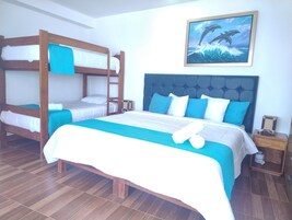 Habitación de hotel con literas, una cama individual y cabecera tapizada. En la pared, un cuadro de delfines.