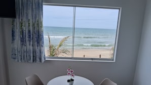 A room with a large window overlooking a beach, a round table with two chairs, and a potted orchid on the table. - Las Fragatas Casa Hotel  (Canoas de Punta Sal)