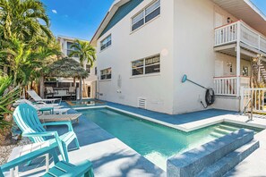A pool area with lounge chairs, a thatched umbrella, and a white building with balconies.