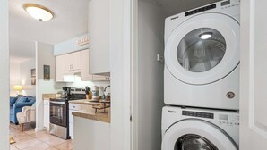 A laundry room with stacked front-loading washers and dryers, a kitchen area with cabinets and a countertop, and a living room with a sofa and a coffee table. - LJ's Cottage 2 - POOL BEACH SUNSETS BALCONY (Sarasota)