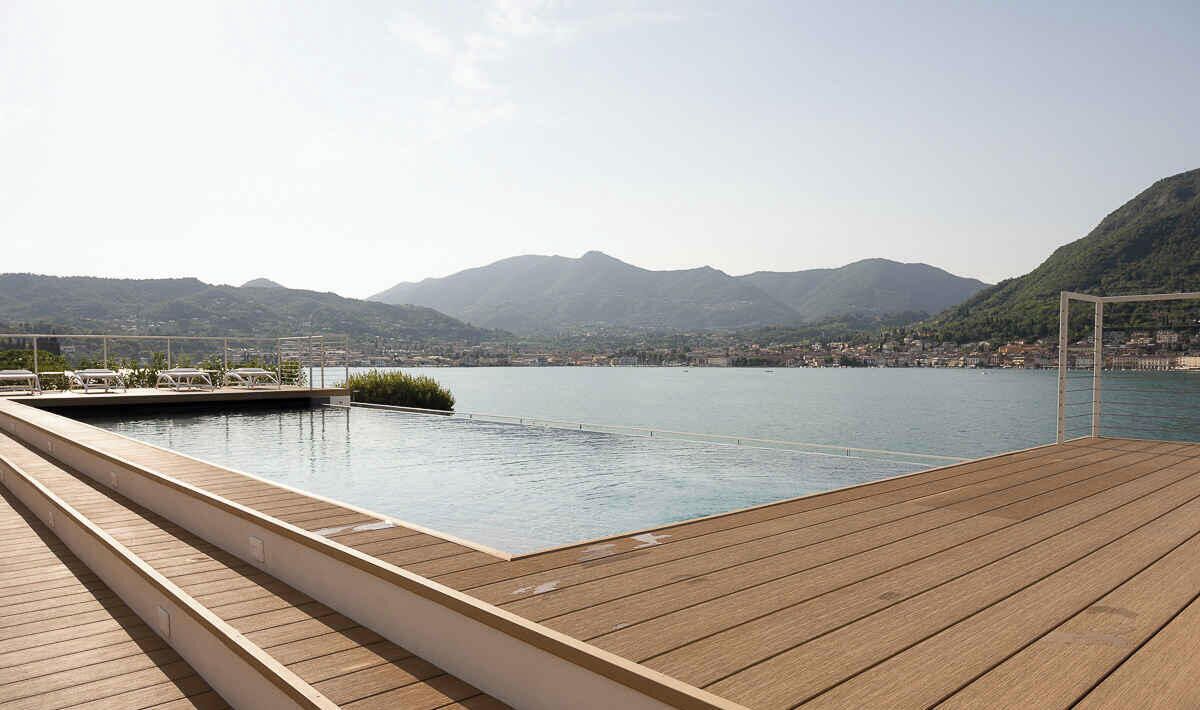 Eine Holzterrasse mit Pool und Blick auf einen See und Berge.