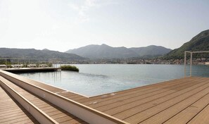 A wooden deck with a pool overlooking a lake and mountains.