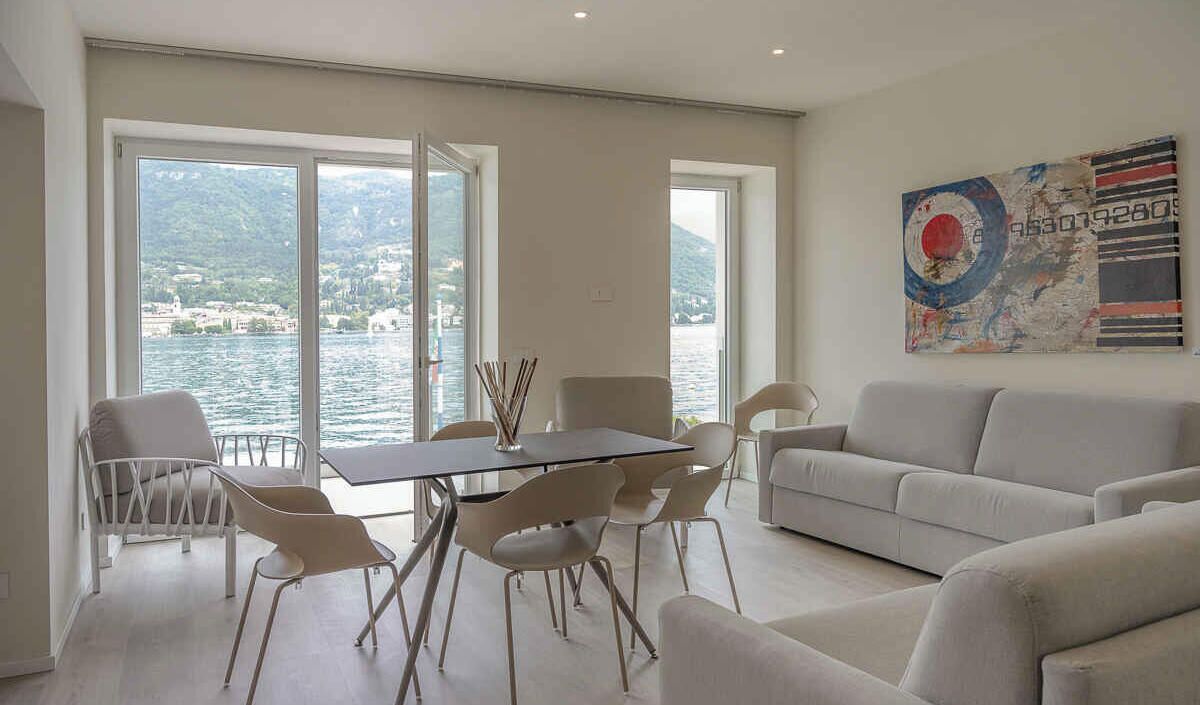 Ein modernes Wohnzimmer mit Seeblick, ein Essbereich mit Stühlen und Tisch sowie eine Sitzecke.