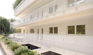 A modern building with a white facade, multiple windows, and a covered outdoor area with greenery.