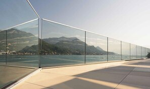 A modern glass railing overlooking a body of water with mountains in the background.