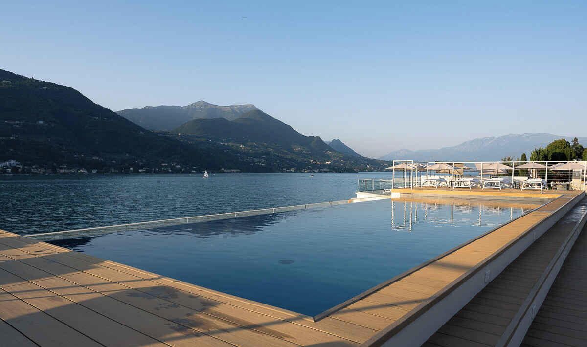 A swimming pool with a wooden deck, overlooking a lake with mountains in the background.