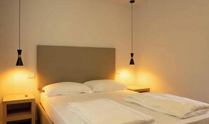 A hotel room with a single bed, two bedside tables, and two pendant lights.