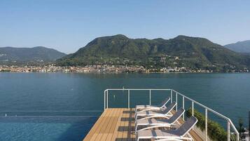 A deck with lounge chairs overlooking a body of water with a mountainous backdrop.