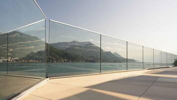 Een moderne glazen balustrade met uitzicht op een wateroppervlak en bergen op de achtergrond.