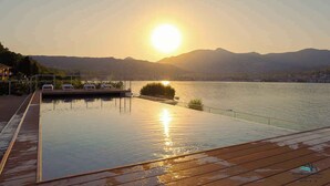 Une piscine à débordement offrant une vue sur un coucher de soleil se reflétant sur une étendue d’eau et des montagnes.