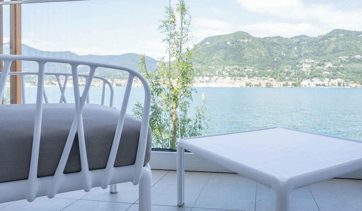 Un balcon avec une chaise en métal blanc et une petite table, donnant sur une étendue d’eau et un paysage vallonné.