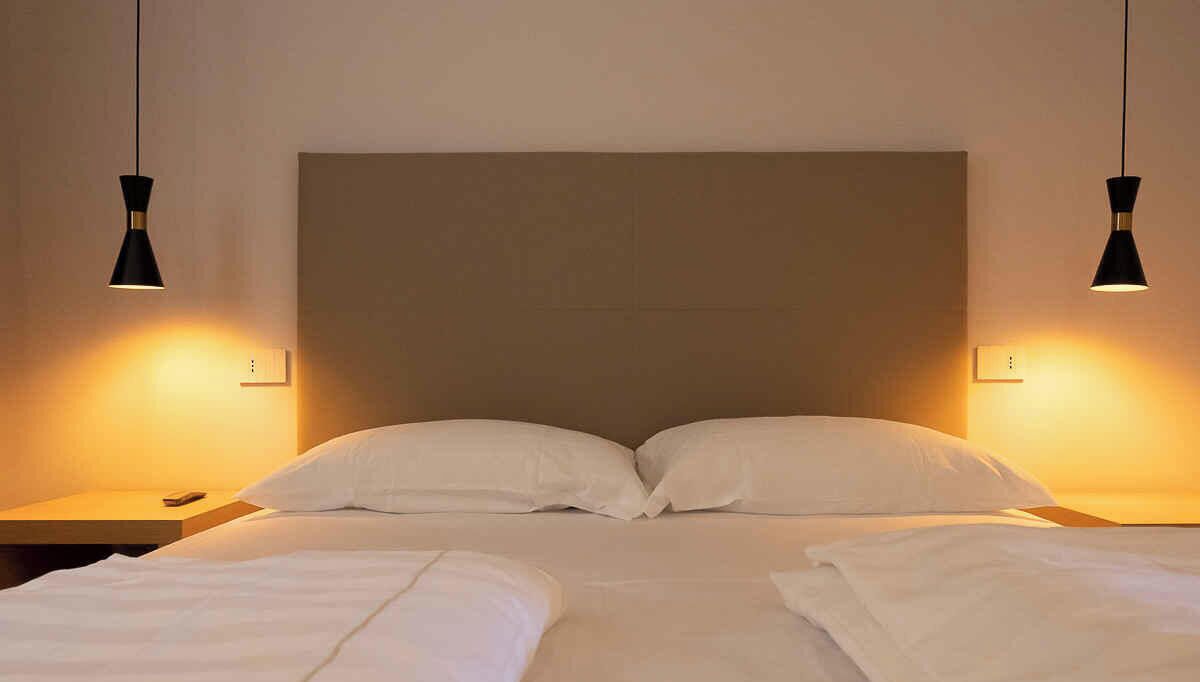 Une chambre d’hôtel avec un grand lit, deux tables de chevet et deux lampes suspendues.