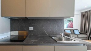 Une cuisine moderne dotée d’un plan de travail en marbre, d’un évier en acier inoxydable et d’une hotte intégrée.