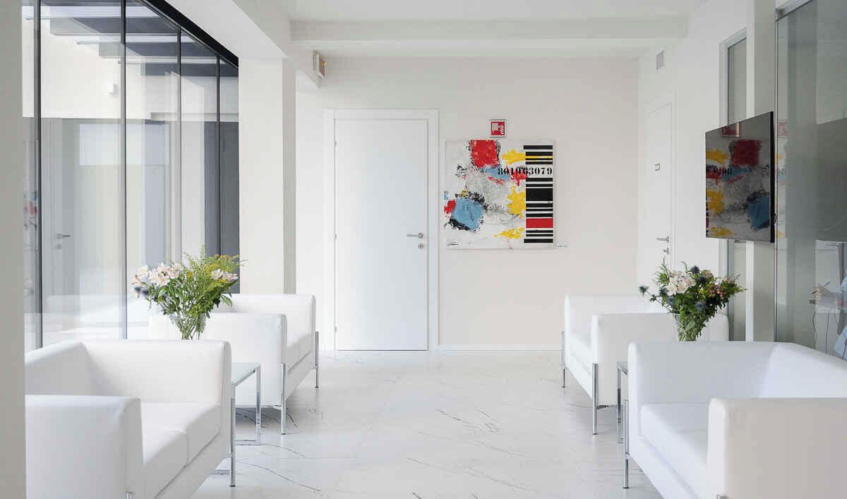 Eine moderne Hotellobby mit weißen Möbeln, einer Glastrennwand und abstrakter Wandkunst.