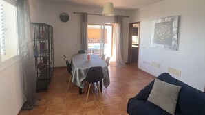 Un soggiorno con un divano blu scuro, un tavolo da pranzo con sedie, un lampadario e una sveglia a muro.