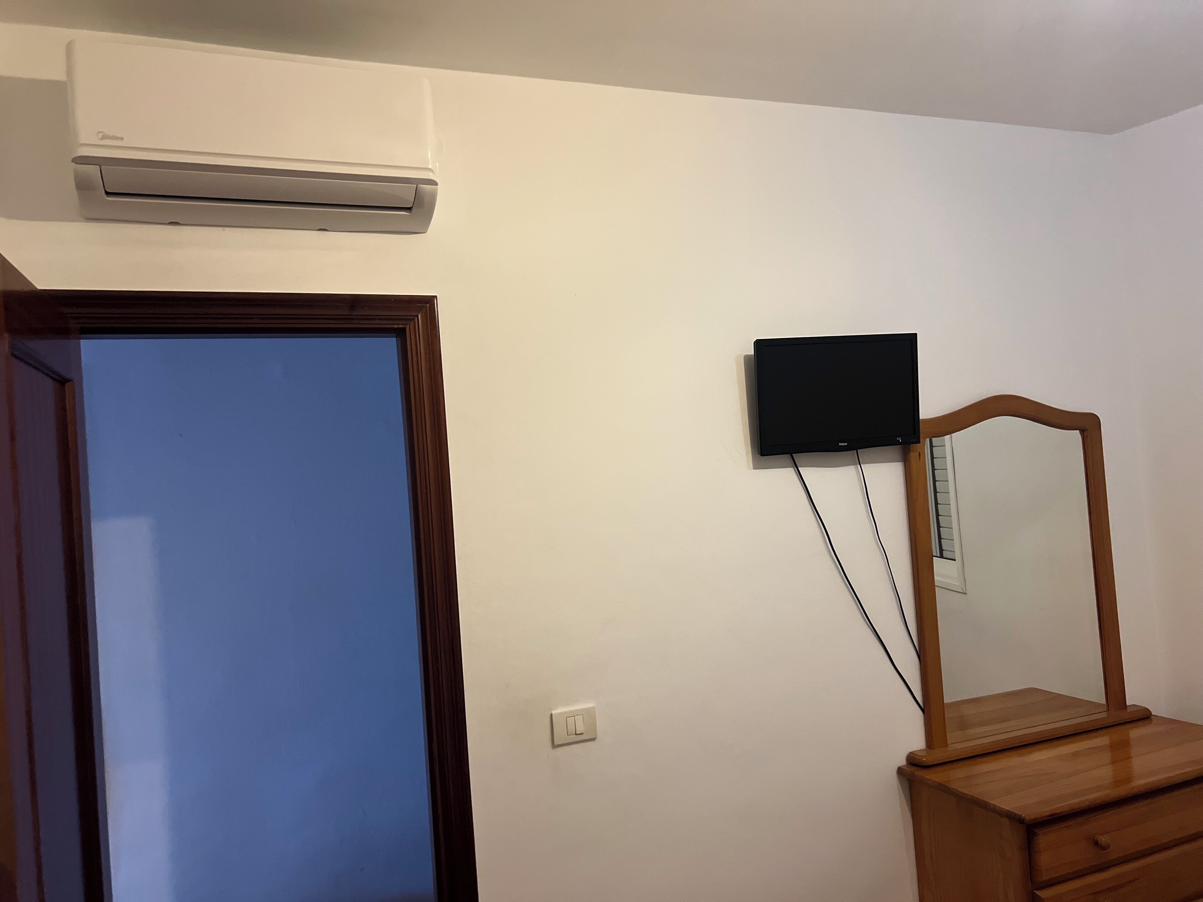 Et værelse med en trækommode, et fladskærms-tv ophængt på væggen og en aircondition-enhed over kommoden.