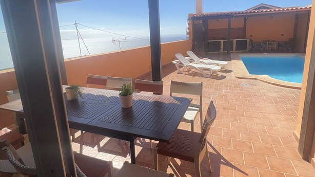 Una terrazza esterna con piscina, poltrone prendisole e un tavolo con sedie.