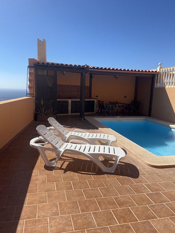 Un área de piscina en la azotea con sillones de descanso y una zona de barbacoa.