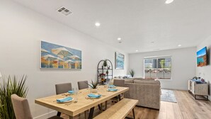 A modern living room with a wooden dining table set for four, a grey sofa, and a large window with a view of a rocky landscape.