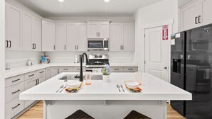A modern kitchen with white cabinetry, a central island, stainless steel appliances, and a black refrigerator.