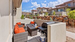An outdoor patio with wicker furniture, a grill, and a stone wall.