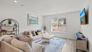 A modern living room with a large window, a sofa set, a coffee table, and a TV mounted on the wall.