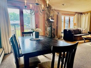 A dining area with a dark wooden table, chairs, and a chandelier. There is a fireplace and a sofa in the background. - RENOVATIONS ALMOST COMPLETE- NEW PHOTOS SOON! Ski-In Ski-Out OberTal F Building! (Stratton)
