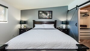 Une chambre à coucher comprenant un lit, des tables de chevet, un tableau et une armoire avec une porte coulissante.