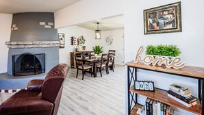 Un salon avec une cheminée, un coin repas et une bibliothèque remplie de livres, ainsi qu’un panneau indiquant « chez soi ».