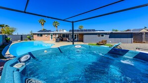Un jardin avec une piscine et un jacuzzi, entouré d’une terrasse couverte.