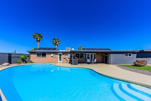 Una casa moderna amb piscina, panells solars i una zona de pati amb mobiliari exterior.