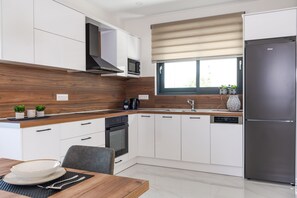 Una cocina moderna con armarios blancos, un refrigerador de acero inoxidable, un microondas y una ventana con persianas.