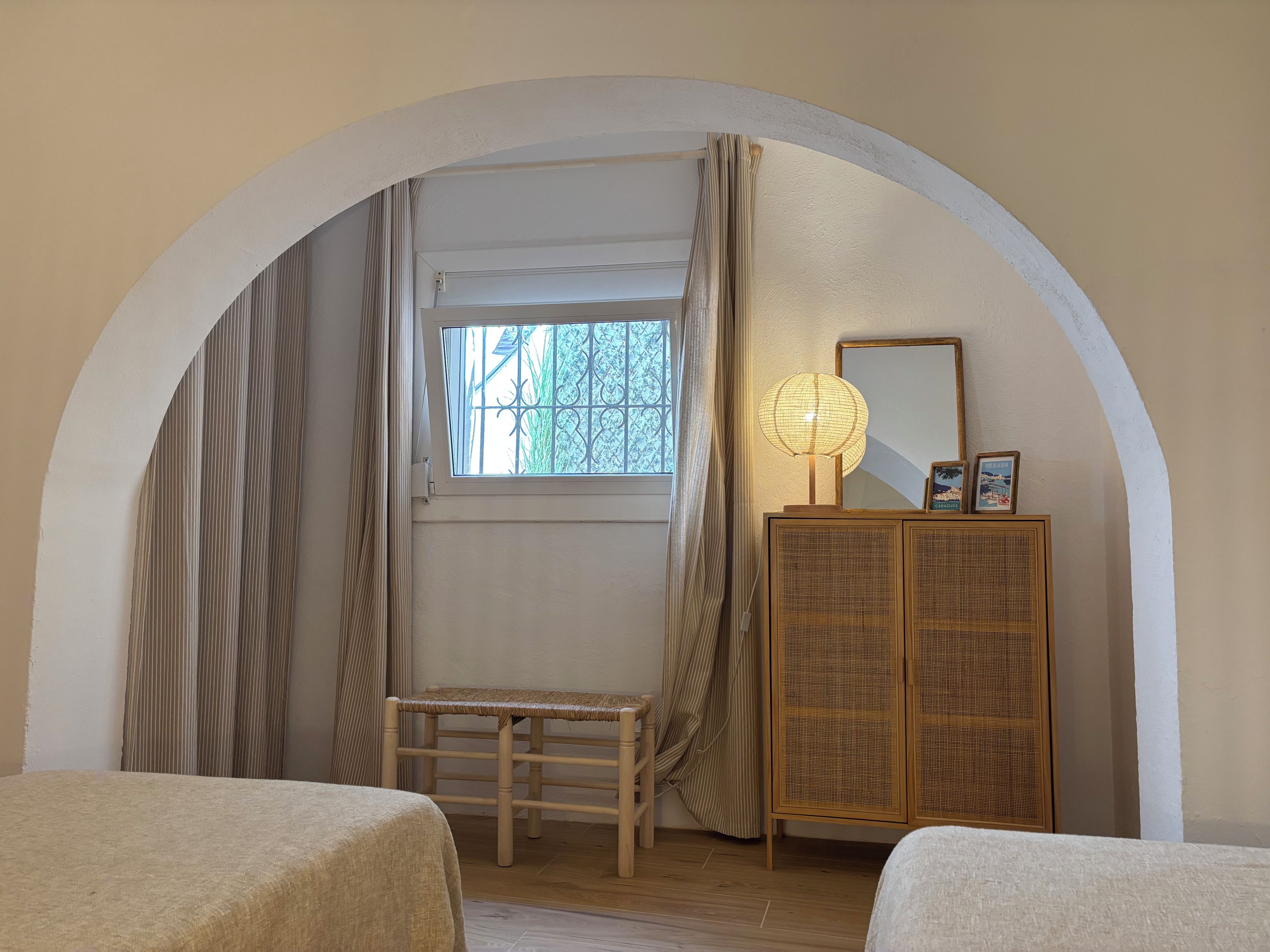 A room with an arched doorway, a bench, a cabinet with a lamp, and a window with curtains.