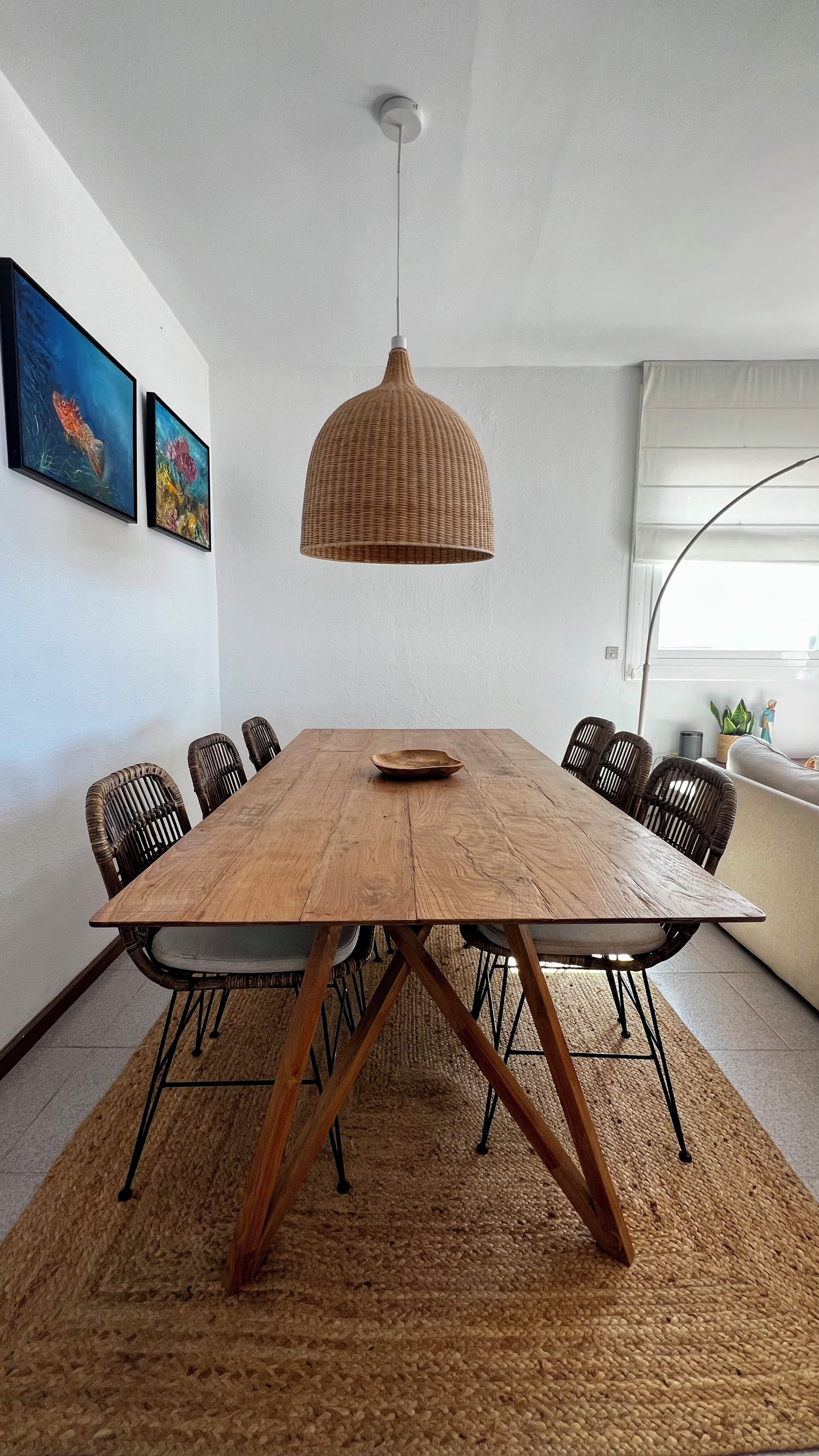 En matplats med ett träbord, svarta stolar, en flätad hänglampa och två inramade konstverk på väggen.