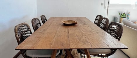 En matplats med ett träbord, svarta stolar, en flätad hänglampa och två inramade konstverk på väggen.