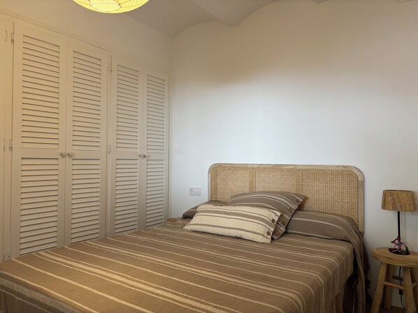 A bedroom with a bed, a bedside table, a lamp, and a wardrobe.