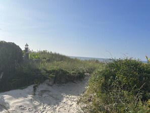 A sandy beach with a lighthouse and dense vegetation.