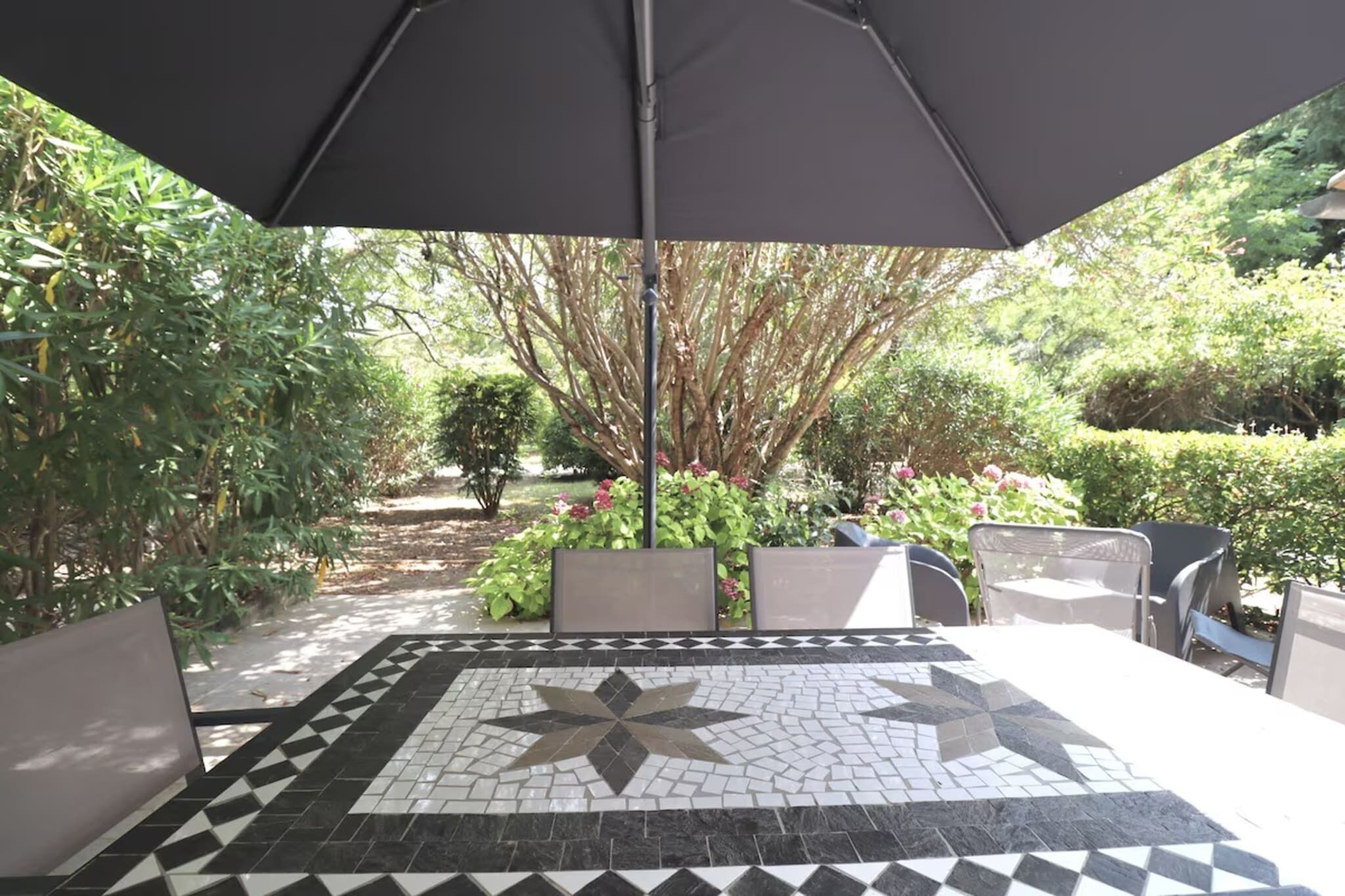 A patio area with a tiled floor, outdoor furniture, and a large umbrella providing shade.
