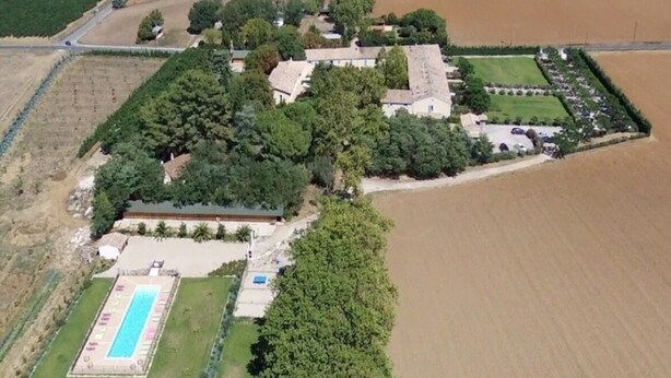 An aerial view of a property with a swimming pool, tennis court, and surrounding greenery.