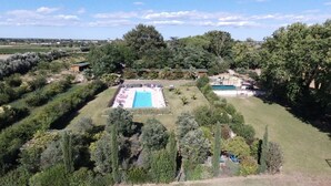 An aerial view of a property with a rectangular swimming pool surrounded by a well-maintained lawn and various trees.