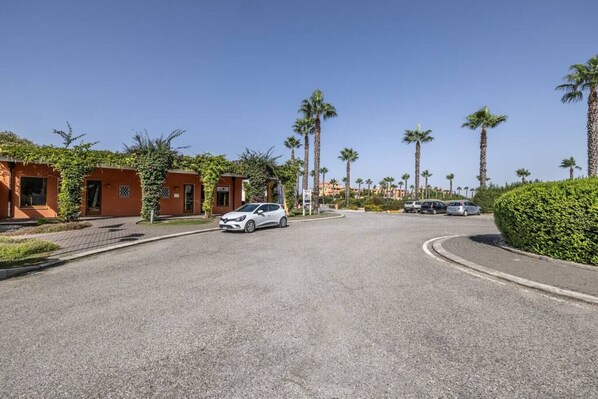 A residential street with a white car parked on the side, palm trees, and houses with brick facades.