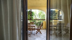 A balcony with wooden chairs and a table, a yellow awning, and a view of greenery.