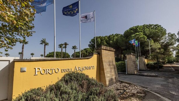 A yellow wall with the text "Porto degli Argonauti" and multiple flags.